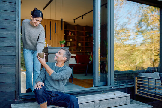 Happy couple interacting, sharing an outdoor coffee moment on a modern home porch during sunny autumn weather