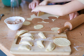 Freshly made dumplings arranged on wooden board with soft light and blurred hands in background. Concept of authentic homemade food, tradition, and cozy kitchen atmosphere with copy space.