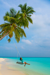 Tranquil closeup calm sea water waves with palm trees. Woman tourist swinging, Tropical island beach landscape exotic shore coast. Summer vacation, holiday amazing nature. Relax paradise, Maldives.