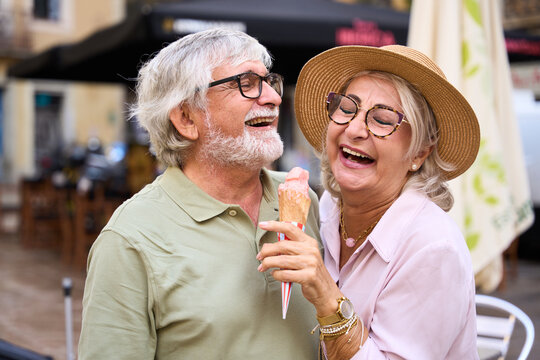 Senior couple sharing ice cream and laughing outdoors - Powered by Adobe