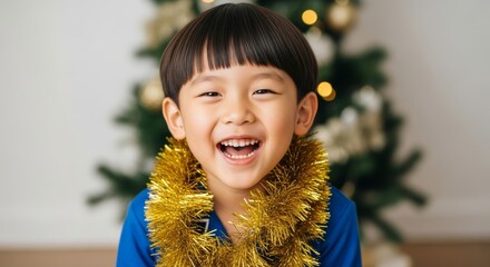 Close-up of a smiling Asian boy wearing a gold tinsel garland, with a softly blurred Christmas tree and warm bokeh lights in the background, bright festive portrait