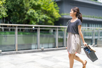 Fototapeta premium Happy asian woman walking outdoors with shopping bags at mall, joyful shopping fashion, consumer happiness, weekend activity and celebrating purchase, sale promotion, cashback reward after shopping