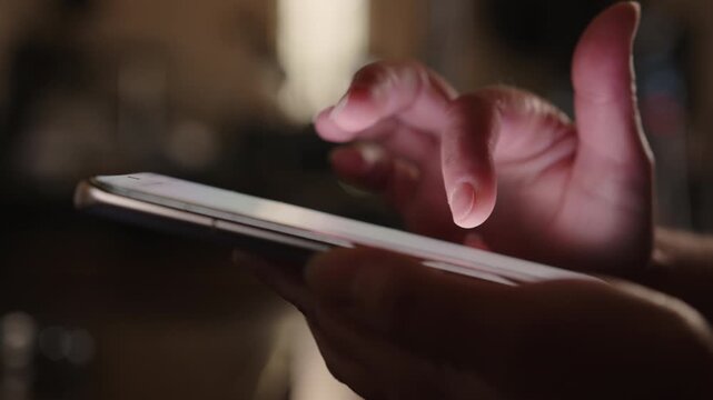 Woman hand using smartphone in room scrolling mobile phone touch screen with finger close up side view