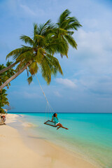 Tranquil closeup calm sea water waves with palm trees. Woman tourist swinging, Tropical island beach landscape exotic shore coast. Summer vacation, holiday amazing nature. Relax paradise, Maldives.
