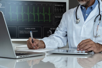 Doctor writing clinical notes while analyzing patient's ECG data on a digital monitor