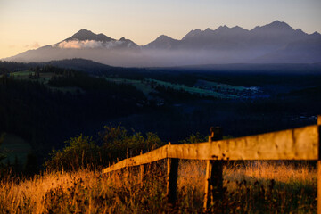 Wschód słońca nad Tatrami, mglisty górski pejzaż z drewnianym ogrodzeniem i złotą trawą na pierwszym planie © Przemysaw