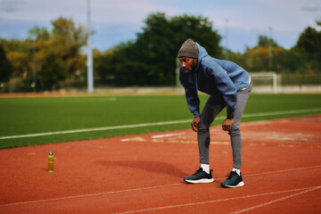 Exhausted male athlete pauses and leans on his knees to catch his breath on a running track after a strenuous outdoor training session.