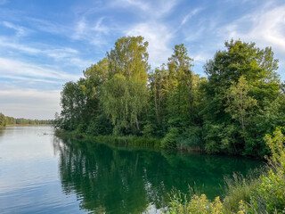 Fototapeta premium Calm forest lake landscape with reflection of green trees in water under blue sky