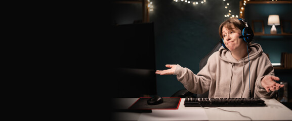 Irritated E-sport female gamer in headphones play online video game with displeased face expression showing dont know gesture while using computer. Confused gaming player broadcast live