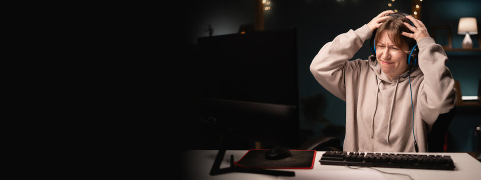 Angry E-sport female gamer in headphones play online video game feeling anger hate while using computer. Young gaming player broadcast live streaming plays video games