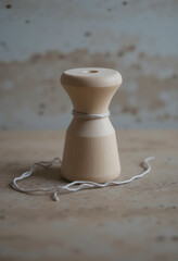 Minimal wooden spool with white string on rustic table in soft natural light