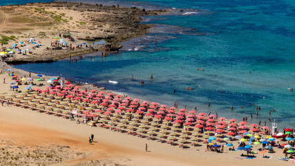 Aerial view of a beach club with red umbrellas. Many vacationers are here on this sunny summer day. This is Macari Beach, located near San Vito Lo Capo, province of Trapani, in Sicily, Italy.