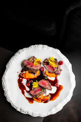 Gourmet dish of sliced beef tenderloin drizzled with dark red sauce, served on a textured white plate with yellow garnish and an orange purée