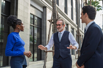 Group of diverse business professionals discussing a project outside an office building. The scene captures leadership, teamwork, strategic planning, and corporate communication in natural daylight.