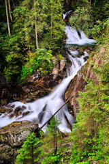 Malowniczy górski wodospad w lesie, długie naświetlanie, czysta natura i spływająca woda wśród skał i świerków © Przemysaw
