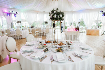 Wide view of a beautifully set round wedding table with an elevated floral centerpiece and a bright banquet hall backdrop, ready for a formal event