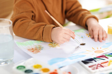 Little boy with brush drawing flowers at white table, closeup