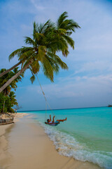Tranquil closeup calm sea water waves with palm trees. Man tourist swinging, Tropical island beach landscape exotic shore coast. Summer vacation, holiday amazing nature. Relax paradise, Maldives.