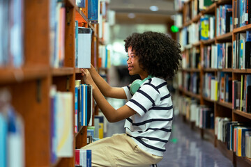 African American young girl finding book and reading book on bookshelf in school library. Education knowledge Concept