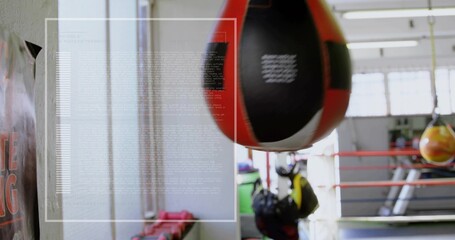 Swinging black and red teardrop punching bag in boxing gym, with ring ropes, gloves, equipment