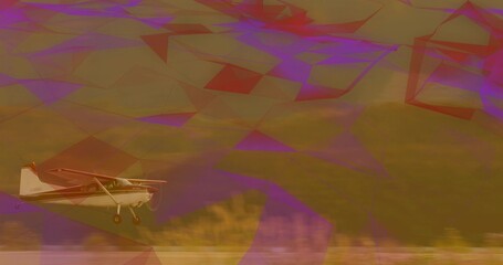 Flying small single-engine propeller airplane skimming grassy field, with landing gear and hillside