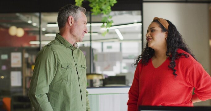 Talking man in green shirt and woman in red sweater at modern open-plan office, with monitor