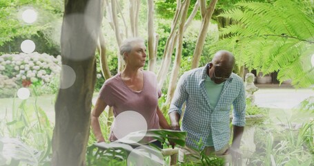 Strolling senior man and mature woman through lush winding garden path, with wooden handrail