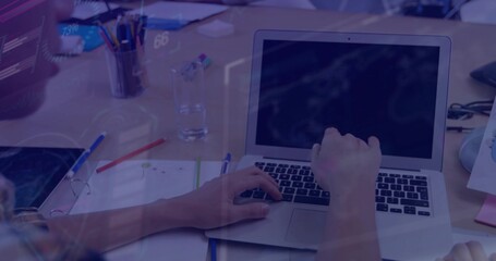 Typing office worker's hands with rolled sleeves on desk in open plan office with laptop documents