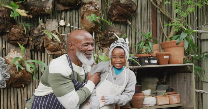 Gardening grandfather and grandson kneeling in backyard garden, with terracotta pots and ferns - Powered by Adobe