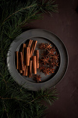 A metal plate containing cinnamon. On the left, pine branches evoke the scents and traditions of Christmas.
