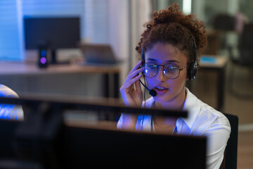 Female customer service agent wearing headsets support and assistance to clients working in call center office at night.