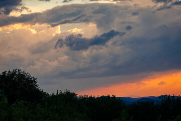 Obraz premium Dramatic evening sky with heavy clouds and warm orange sunset light over mountain landscape