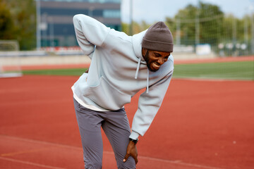 Male athlete cries out in pain, holding his lower back with his hand due to a serious injury or muscle cramp during a break in his outdoor workout