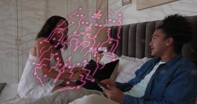 Woman entering bedroom joining man reviewing tech tablet showing pink pattern laughing and hugging