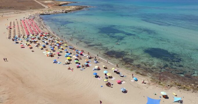 Aerial view of vacationers on a sandy beach with colorful umbrellas. This is Macari Beach, located near San Vito Lo Capo in Sicily, Italy. It's a public beach.
