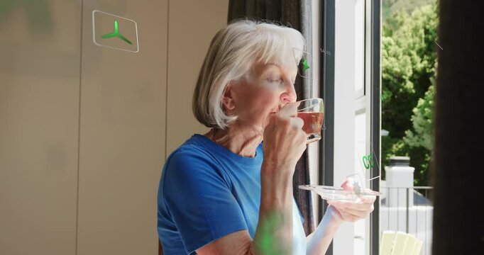 Senior woman lifting teacup by glass door and monitoring air quality icons shifting around her