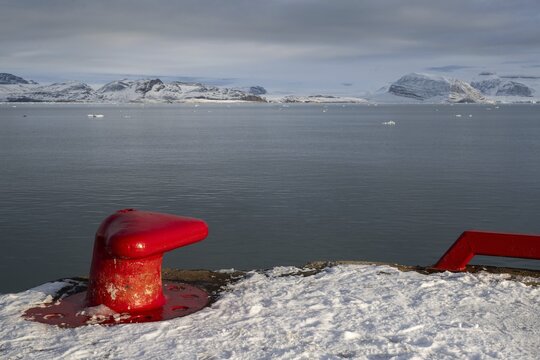 Red bollard in front of the wintry, snow-covered Kongsfjorden, harbour, Ny-&Aring;lesund, Spitsbergen Island, Svalbard and Jan Mayen archipelago, Norway