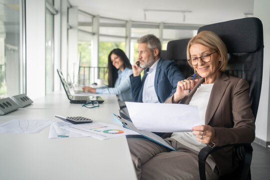 Three busy happy middle aged professional business man and two women executive leaders team using laptop working on computer at work desk having conversation on financial project at meeting in office.