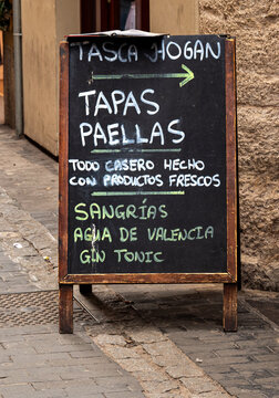 VALENCIA, SPAIN &ndash; NOVEMBER 1, 2025: Rustic handwritten sign near Plaza Redonda in Valencia, Spain, advertising traditional tapas, agua de Valencia  and paellas in a historic urban setting.