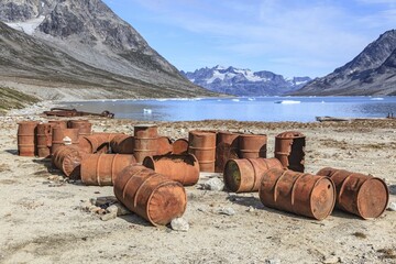Rusted oil barrels on a fjord in front of steep mountains, remains of a US airbase from the Second World War, Ikateq Fjord, East Greenland, Greenland