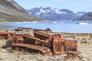 Rusty cars and barrels on a fjord in front of steep mountains, remains of a US airbase from the Second World War, Ikateq Fjord, East Greenland, Greenland