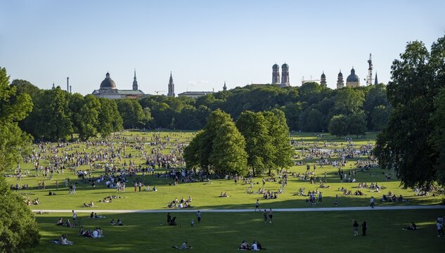 View from the Monopteros in the English Garden, meadows full of visitors on a summer day, Munich city view with dome of the state chancellery, towers of the Church of Our Lady and Theatine Church, Munich, Bavaria, Germany