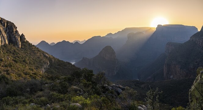 Light mood at sunrise at the Blyde River Canyon, sun rises behind a mountain peak, canyon landscape with sunbeams against the light, view of canyon with Three Rondawels peak and Table Mountains, Panorama Route, Mpumalanga, South Africa