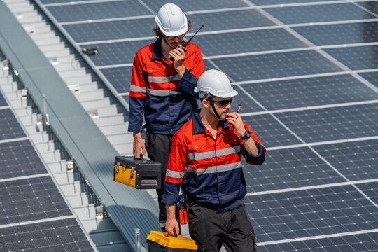 Solar engineer teamwork maintenance energy rooftop technician with helmet tool box radio communication inspection under sunlight on panel field showing focus and safety during routine service - Powered by Adobe