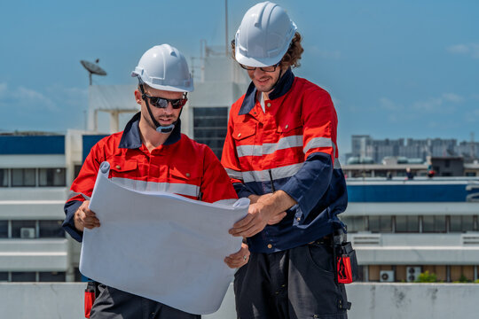 Solar engineer teamwork maintenance energy plan unfolds rooftop as two workers review blueprint bright sky, focused collaboration guides panel inspection and site safety check with professional