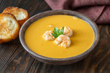 Rustic shrimp bisque with toasted baguette slices beside clay bowl