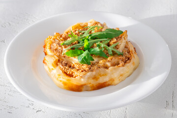 Circular lasagna presentation topped with fresh arugula served on elegant white plate