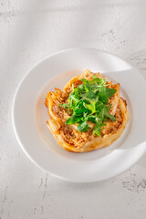 Circular lasagna presentation topped with fresh arugula served on elegant white plate