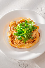 Circular lasagna presentation topped with fresh arugula served on elegant white plate