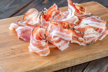 Rustic presentation of sliced Italian pancetta arranged neatly on wooden cutting board